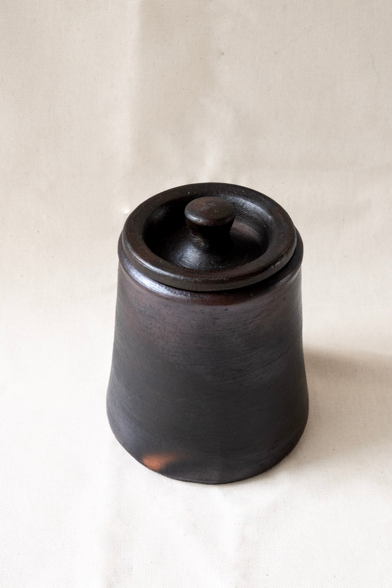 Black ceramic jar with lid on a white background