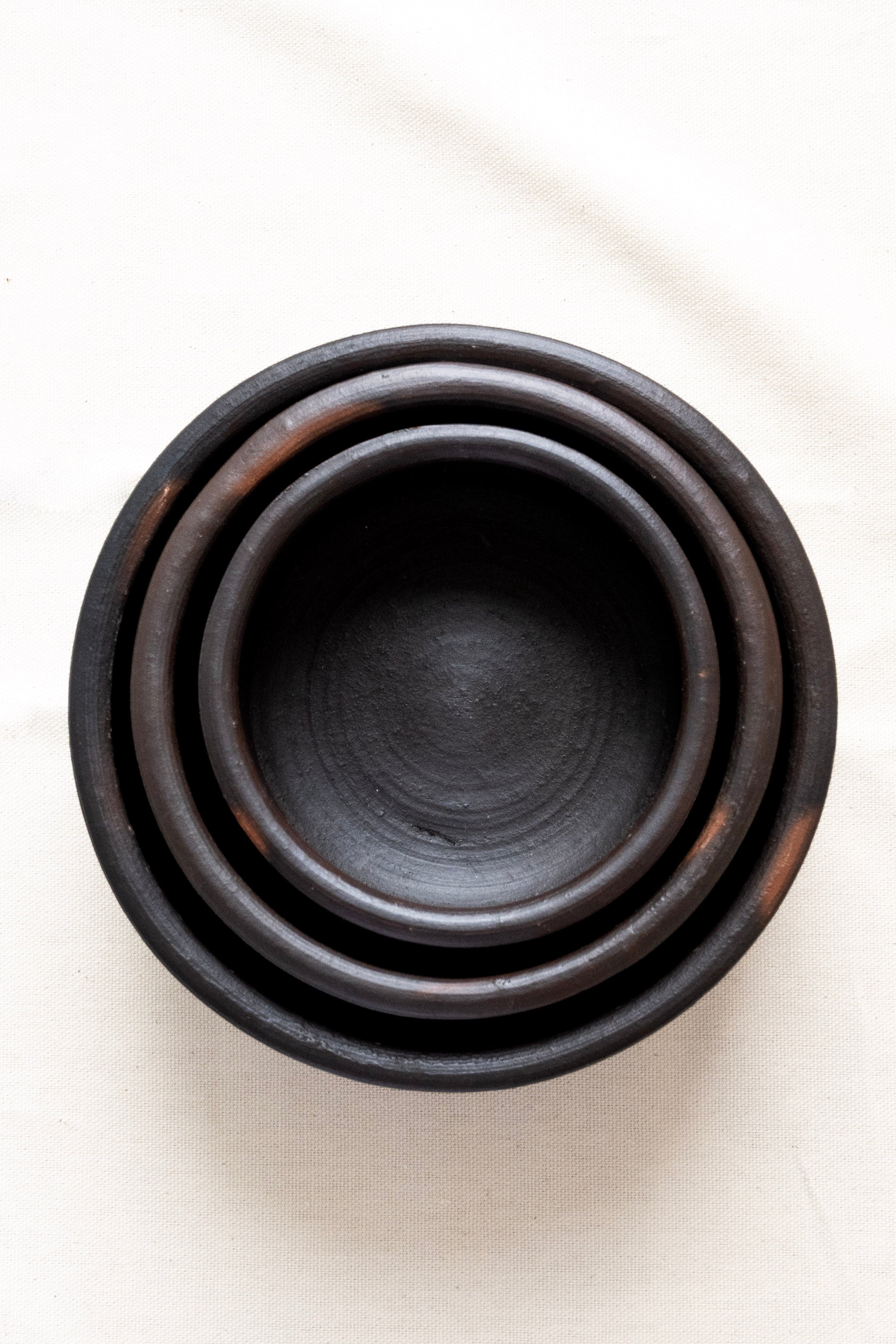 Set of three black ceramic bowls stacked on a white surface