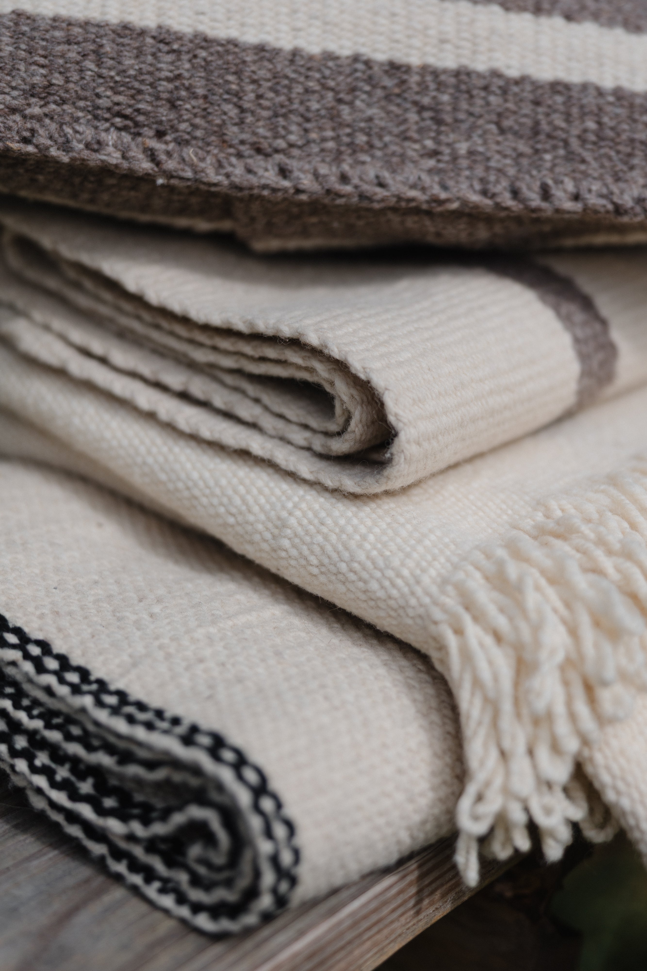 Stack of folded handwoven wool blankets with different patterns and colors on a wooden surface.