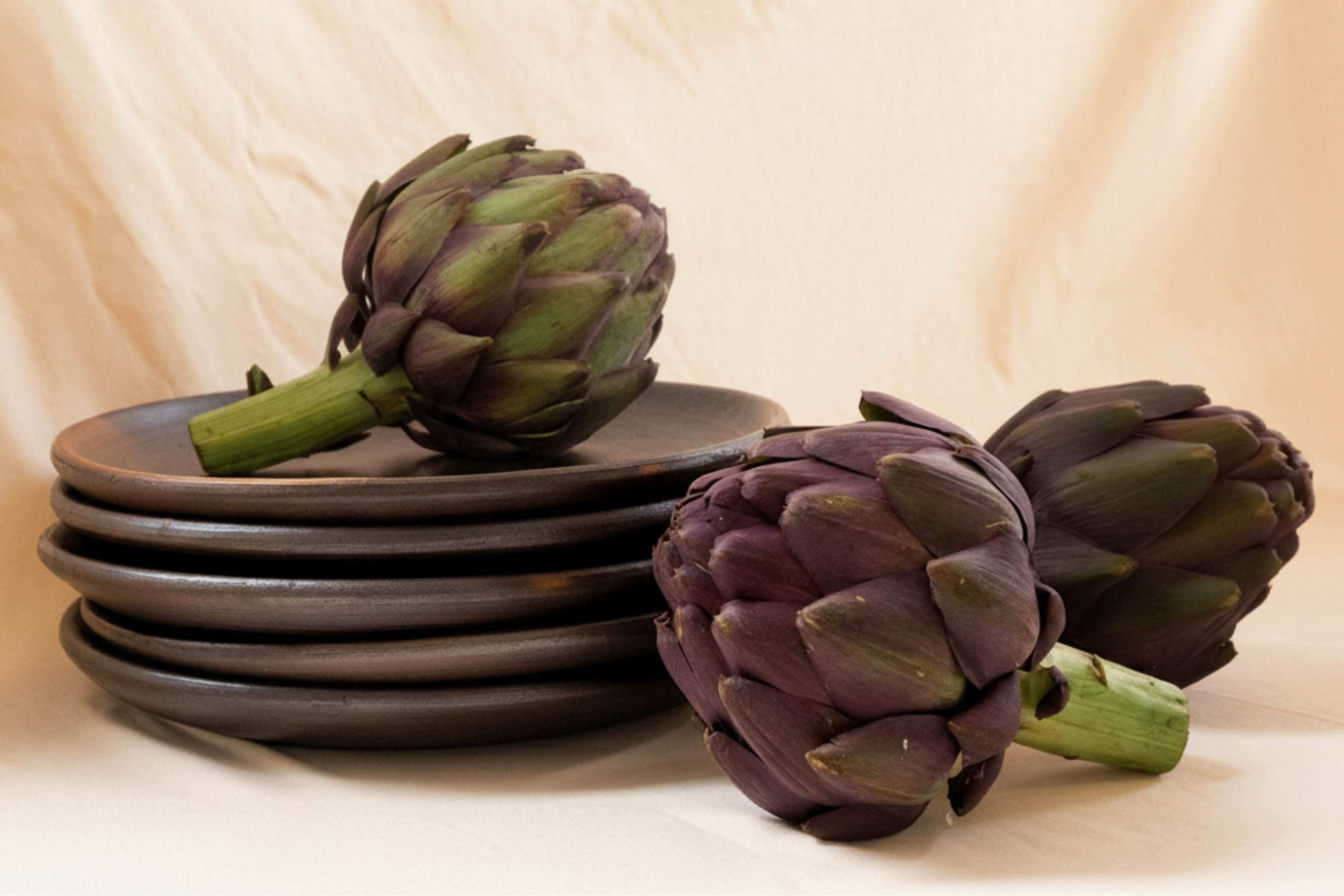 A stack of handmade black clay plates adorned with artichokes.